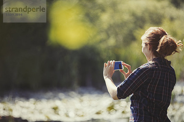 Frau mit Fotohandy am sonnigen Seeufer