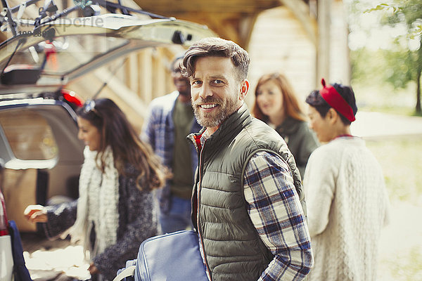 Portrait lächelnder Mann mit Freunden beim Entladen des Autos