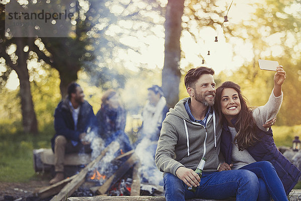 Lächelndes Paar nimmt Selfie mit Fotohandy am Lagerfeuer mit.