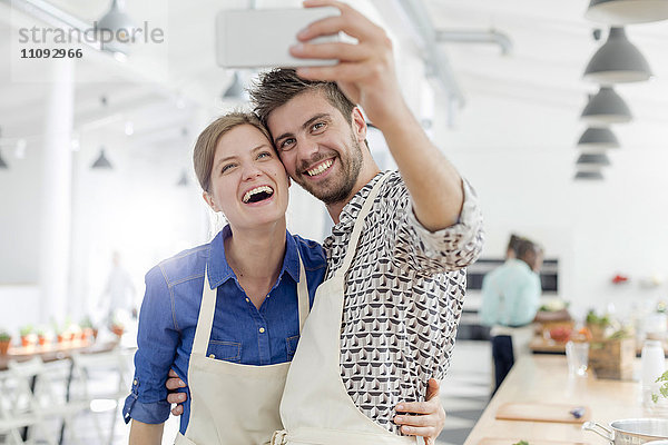 Enthusiastisches Paar nimmt Selfie mit Fotohandy in der Küche des Kochkurses mit