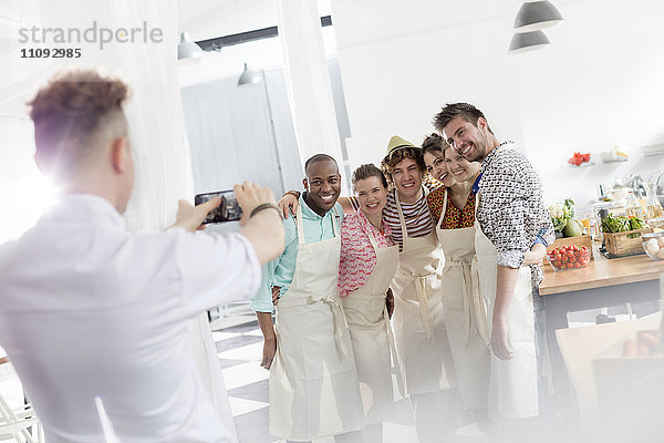 Kochlehrer fotografiert Schüler mit Fotohandy in der Küche des Kochkurses