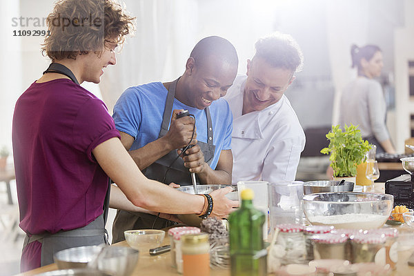 Kochlehrer und Schüler mit Handmixer in der Küche des Kochkurses