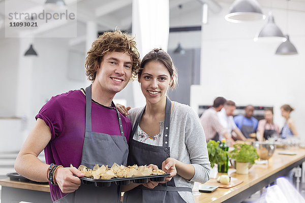 Portrait lächelndes Paar mit Tablett mit Essen in der Küche des Kochkurses