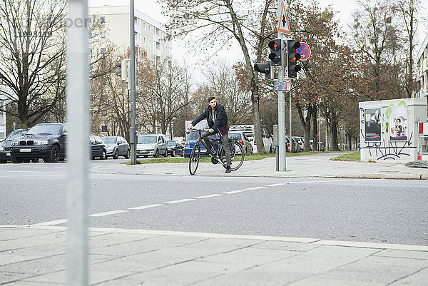 Junger Mann mit Fahrrad in der Stadt beim Warten an der roten Ampel