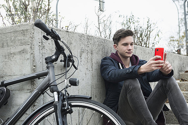 Junger Mann schreibt eine SMS auf seinem Handy und lehnt sich an die Wand