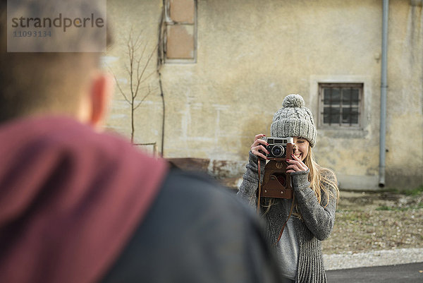 Teenager-Mädchen fotografiert ihren Freund mit einer Kamera im Retro-Stil