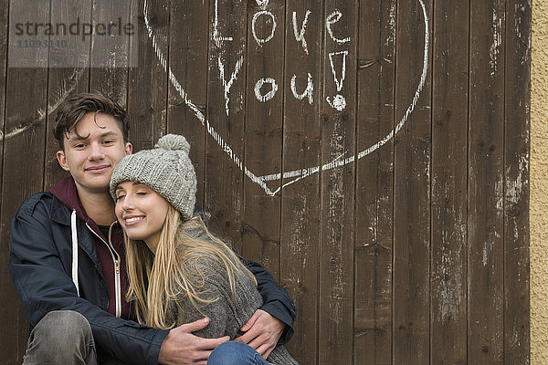 Junges Paar umarmt mit einem gezeichneten Herz und Liebe dich auf eine Holzwand geschrieben