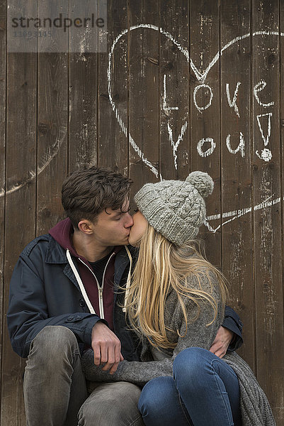 Junges Paar küssen mit einem gezeichneten Herz und Liebe Sie auf einer Holzwand geschrieben