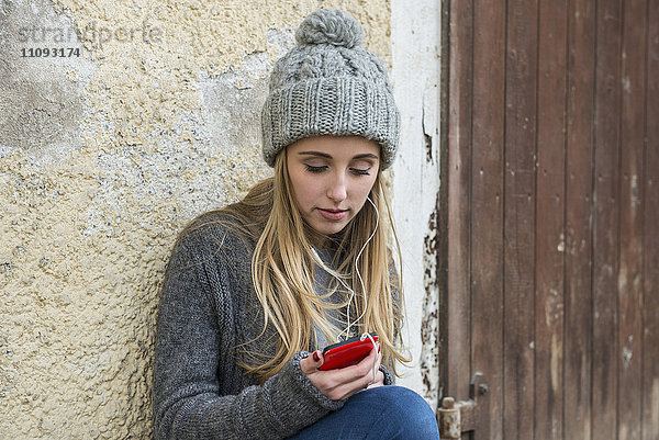 Teenager-Mädchen hört Musik auf dem Mobiltelefon und lehnt sich an die Wand