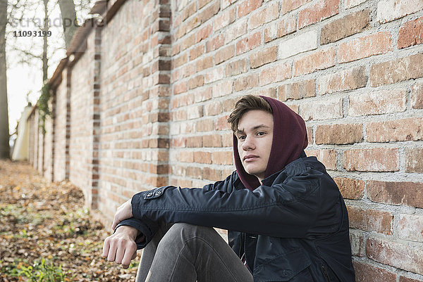 Junger Mann sitzt an einer Backsteinmauer und denkt nach