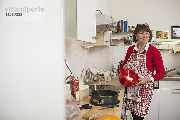 Porträt einer älteren Frau  die in einer Rührschüssel in der Küche Butter rührt