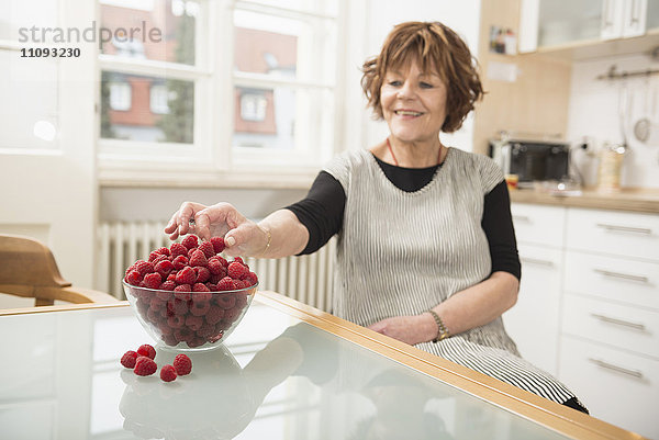 Ältere Frau nascht Himbeeren in der Küche