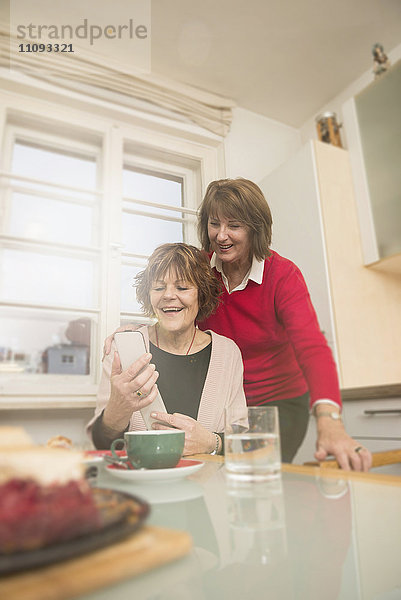 Zwei ältere Frauen benutzen ein Smartphone in der Küche