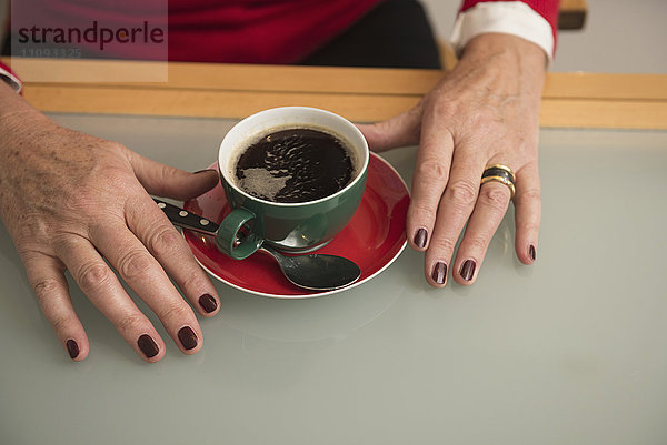 Nahaufnahme der Hand einer älteren Frau und schwarzer Kaffee auf dem Tisch