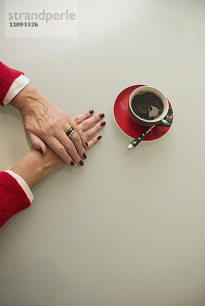 Nahaufnahme der Hand einer älteren Frau und schwarzer Kaffee auf dem Tisch