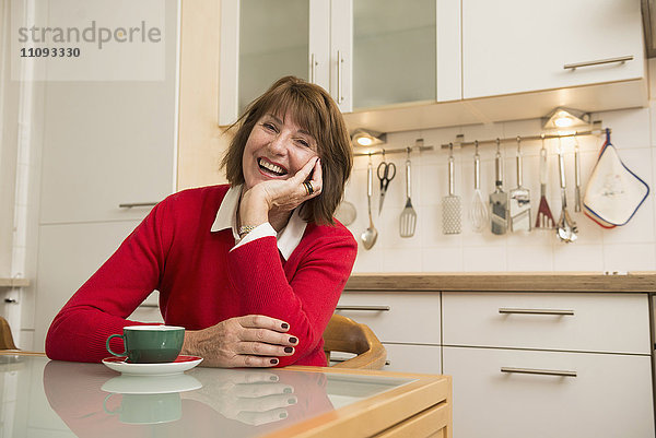 Porträt einer älteren Frau  die in der Küche sitzt und lächelt