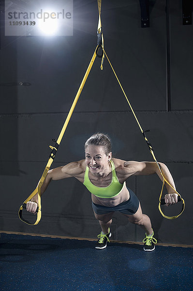 Sportliche Frau macht Liegestütze mit TRX-Gürtel im Fitnessstudio