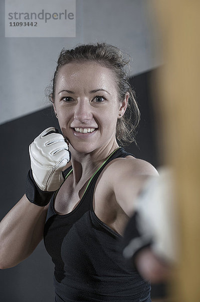 Junge Frau macht Krafttraining  indem sie auf einen Boxsack im Fitnessstudio schlägt