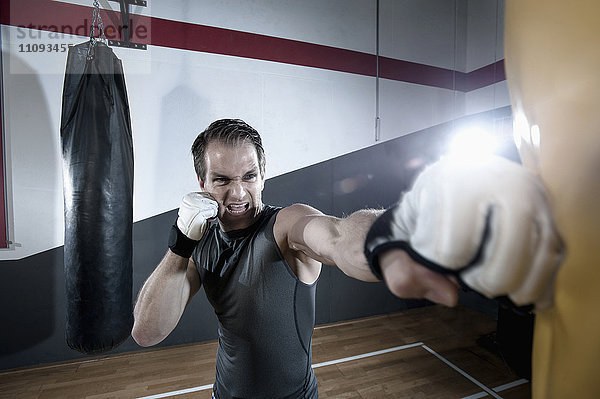 Sportler beim Krafttraining mit einem Boxsack im Fitnessstudio