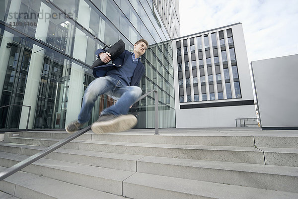 Glücklicher Teenager  der nach der Arbeit mit seinem Laptop über das Geländer springt