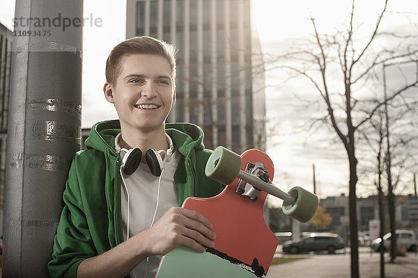 Teenager mit Skateboard  der an einer Stange steht und auf jemanden auf der Straße wartet