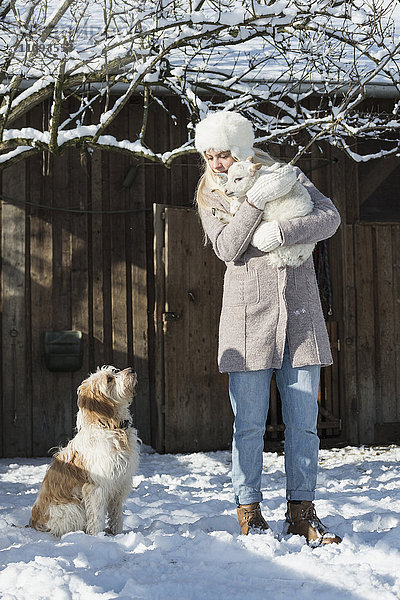 Jugendliches Mädchen vor einer Scheune mit Lamm und Hund im Winter  Bayern  Deutschland