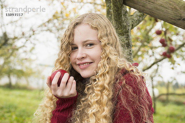 Porträt eines blonden Teenagers  der einen Apfel in einem Apfelgarten isst