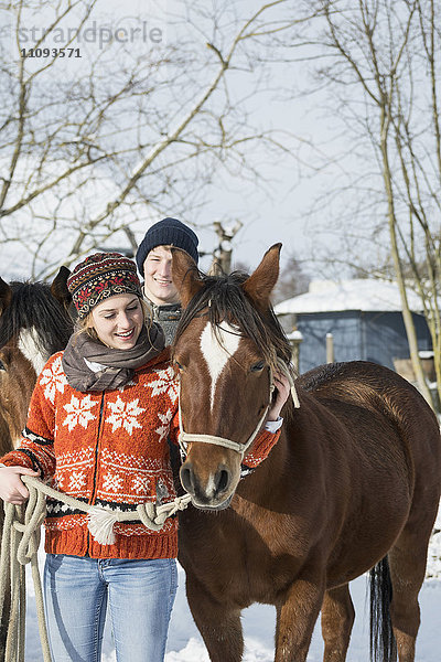 Junges Paar steht mit Pferden in einer Scheune  Bayern  Deutschland