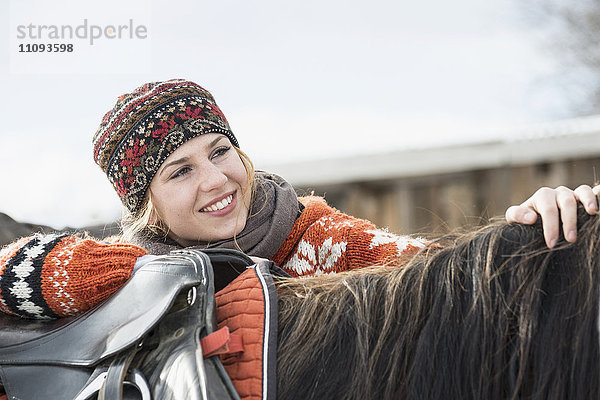 Junge Frau lehnt sich lächelnd auf den Rücken eines Pferdes  Bayern  Deutschland