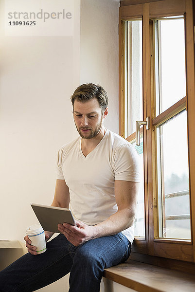 Architekt sitzt auf der Fensterbank und arbeitet an einem digitalen Tablet  Bayern  Deutschland