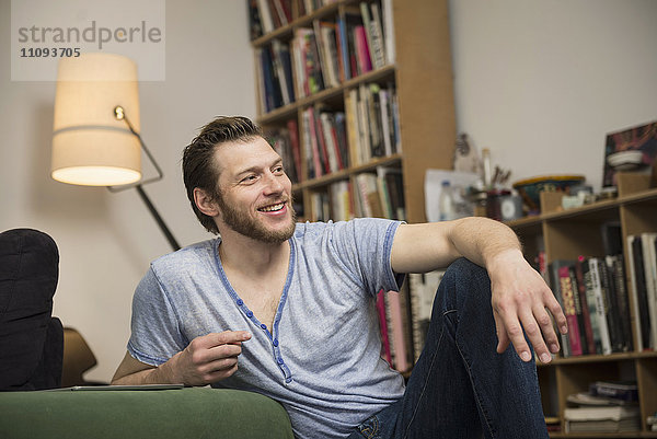 Mittlerer erwachsener Mann  der sich im Wohnzimmer entspannt und lächelt  München  Bayern  Deutschland