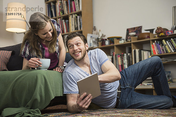 Paar  das im Wohnzimmer ein digitales Tablet benutzt und lächelt  München  Bayern  Deutschland