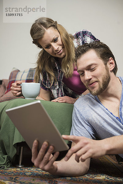 Paar  das im Wohnzimmer ein digitales Tablet benutzt und lächelt  München  Bayern  Deutschland