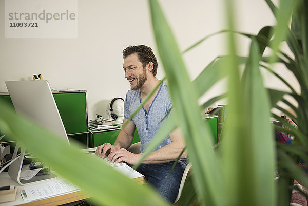 Mittlerer erwachsener Mann  der im Wohnzimmer am Computer arbeitet und lächelt  München  Bayern  Deutschland