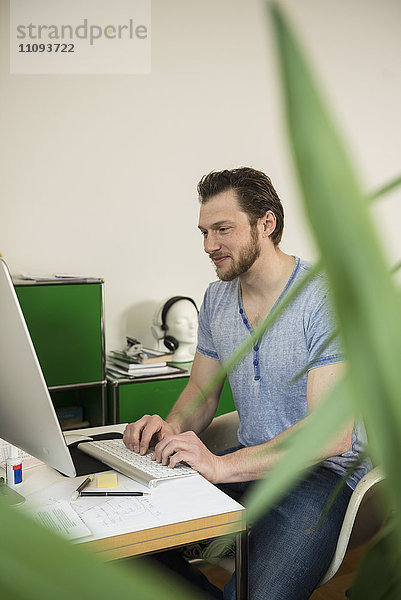 Mittlerer erwachsener Mann arbeitet im Wohnzimmer am Computer und lächelt  München  Bayern  Deutschland