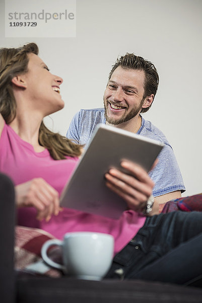 Paar  das im Wohnzimmer ein digitales Tablet benutzt und lächelt  München  Bayern  Deutschland