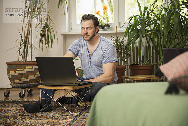 Mittelgroßer erwachsener Mann arbeitet an einem Laptop im Wohnzimmer  München  Bayern  Deutschland