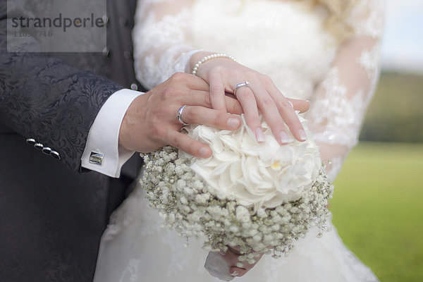 Mittelschnittansicht eines Brautpaares  das einen Blumenstrauß hält und seinen Ehering zeigt