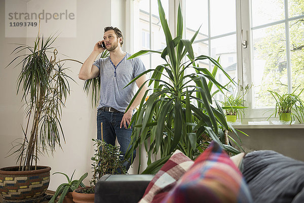 Mittlerer erwachsener Mann  der im Wohnzimmer mit einem Mobiltelefon spricht  München  Bayern  Deutschland