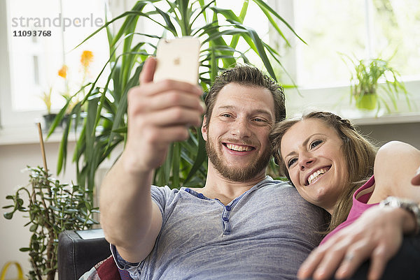 Paar macht Selfie im Wohnzimmer und lächelt  München  Bayern  Deutschland