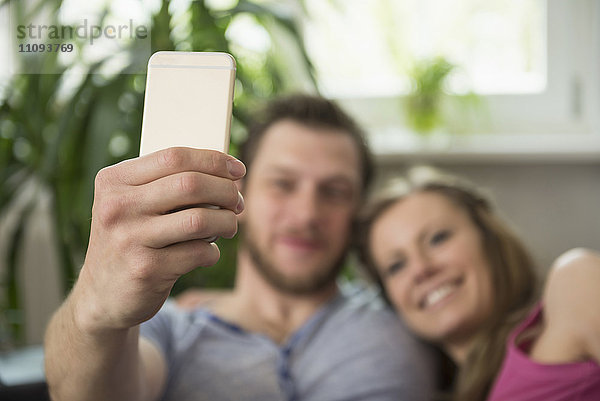 Paar macht Selfie im Wohnzimmer und lächelt  München  Bayern  Deutschland