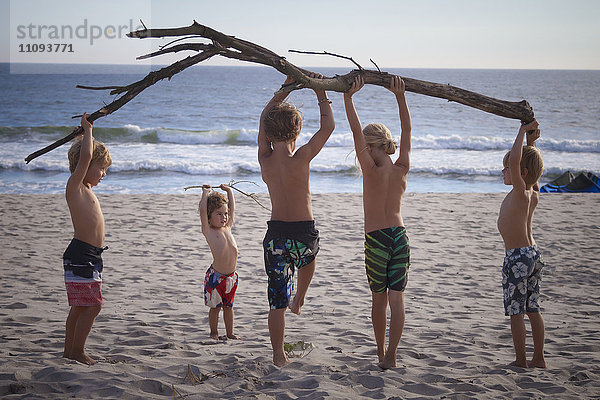 Eine Gruppe von Kindern hält einen Baumstamm am Strand hoch