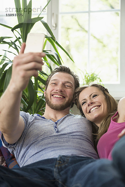 Paar macht Selfie im Wohnzimmer und lächelt  München  Bayern  Deutschland