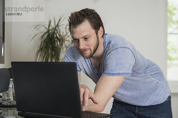 Mittelgroßer erwachsener Mann arbeitet an einem Laptop im Wohnzimmer  München  Bayern  Deutschland