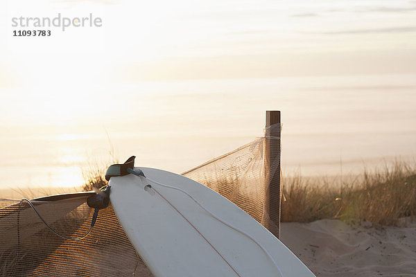 Upside down Surfbrett lehnt gegen Zaun bei Sonnenuntergang