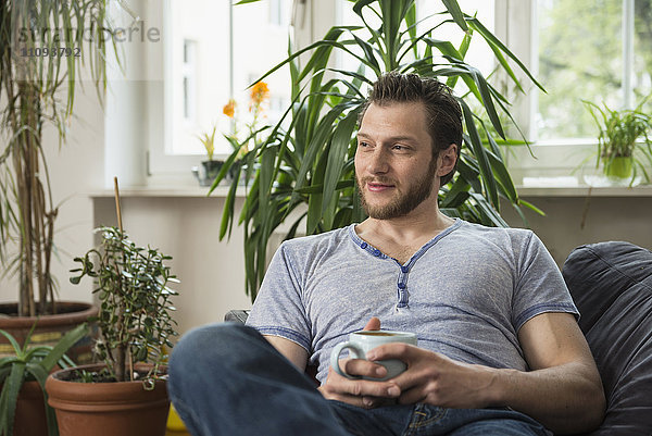 Nachdenklicher erwachsener Mann trinkt Kaffee im Wohnzimmer und denkt nach  München  Bayern  Deutschland