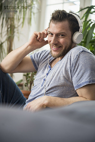 Mittlerer erwachsener Mann hört Musik im Wohnzimmer  München und lächelnd  Bayern  Deutschland