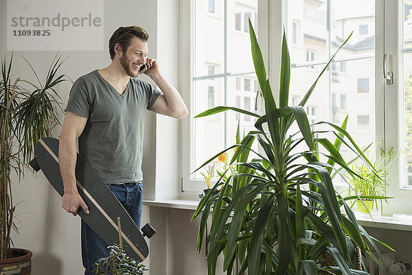Mittlerer erwachsener Mann  der im Wohnzimmer mit einem Mobiltelefon spricht  München  Bayern  Deutschland