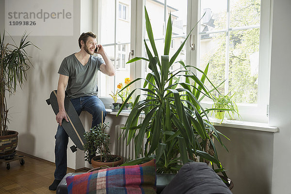 Mittlerer erwachsener Mann  der im Wohnzimmer mit einem Mobiltelefon spricht  München  Bayern  Deutschland