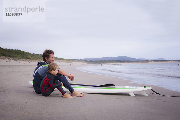 Vater mit Sohn  der am Strand sitzt und die Aussicht genießt